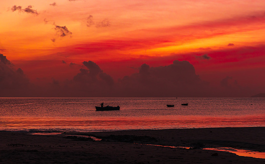 Panoramic night beach landscape, anchored boats are under red tropical sky at sunset. Mahe island, Seychelles