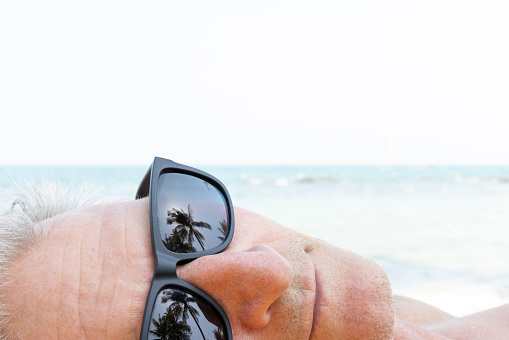 Portrait side profile of senior man relaxing on beach wearing sunglasses