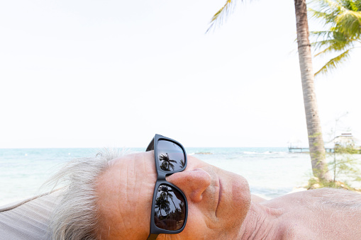 Side profile of senior man wearing sunglasses relaxing under palm tree