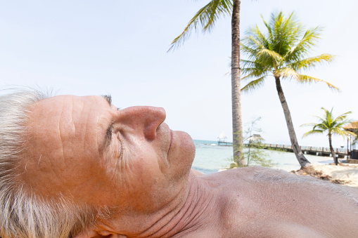 Portrait side profile of senior man relaxing on beach under palm tree