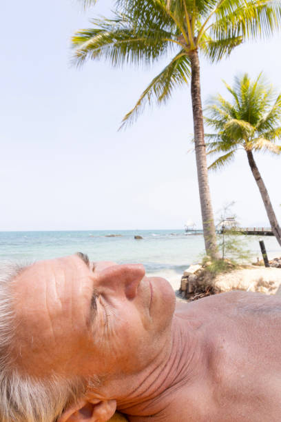 Portrait of senior man relaxing on beach Portrait side profile of senior man relaxing on beach under palm tree vietnamese old man portrait stock pictures, royalty-free photos & images