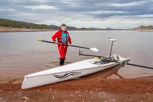 Loveland, CO, USA - February 6, 2024: Senior rower is rigging his Liteboat rowing shell on a shore of Carter Lake in northern Colorado in winter scenery.