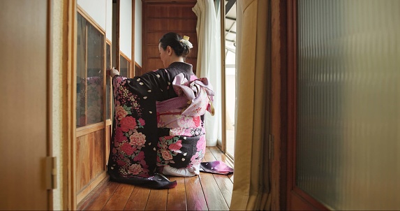 Open door, Japanese woman and culture with hospitality, respect and relax in traditional accommodation. Morning, home and kneel at a window with zen, calm and ancient architecture with antique dress
