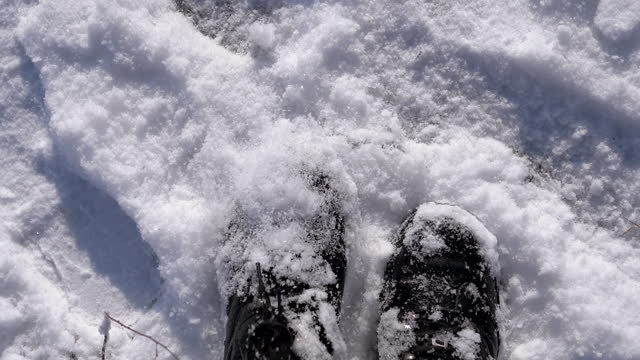 Top View Woman Shakes Snow Off Black Boots While Standing in a Snowdrift in Snow