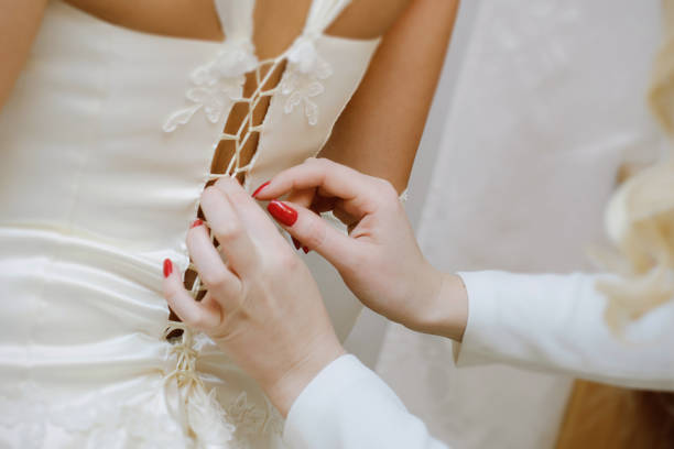 istock Bridesmaids help the bride put on her wedding dress 1993153314