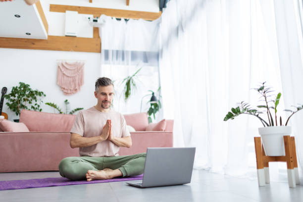 istock Mid adult man practicing yoga at home online using laptop 1993165650