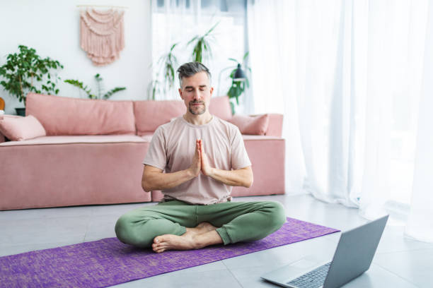 istock Mid adult man practicing yoga at home online using laptop 1993165896