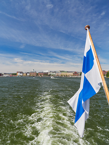 Vertical panorama of European Helsinki, view from the sea, blue sky, national flag of Finland.