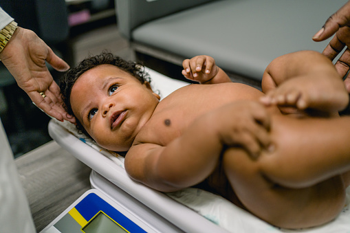 Pediatrician weighing adorable multiracial baby boy on scale in her office