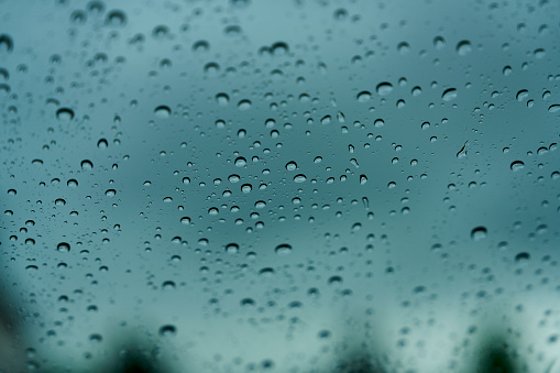 Rain drops on window glass outside texture background water of wonderful heavy rainy day with sky clouds at city blue green blurred lights abstract view sunshine enjoy the relaxing nature wallpaper