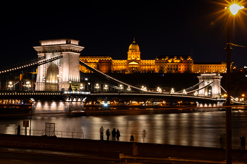 Budapest, Hungary - December 30, 2023: Chain Bridge, Buda Castle, historic, lights, night, illuminated, tourists, Danube, Pest