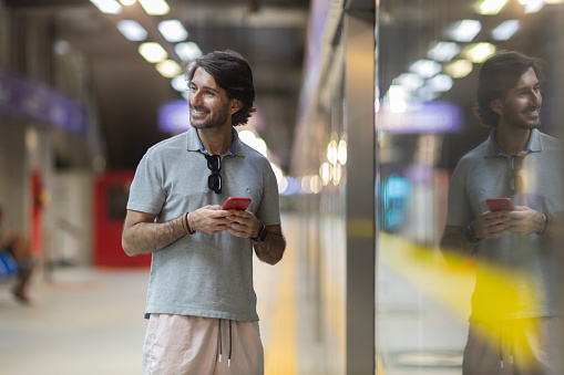 View of young man using a smartphone inside a subway - metro station with a blurred view landscape in the background. High quality photo. Texting on the phone.
