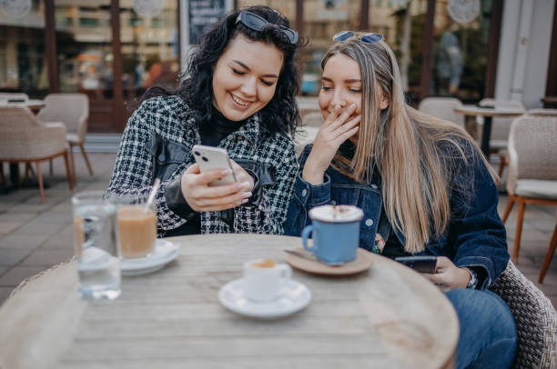 istock Two young woman having coffee while sitting outside at cafe and using mobile phone 1993240519