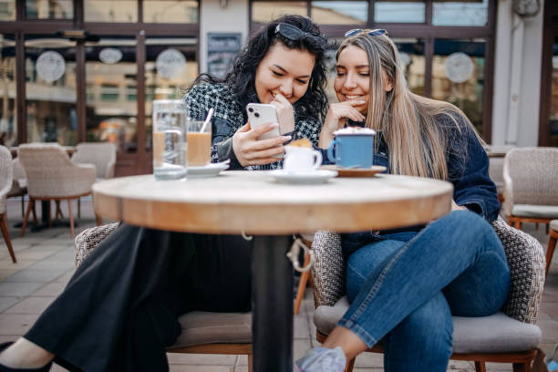istock Two young woman having coffee while sitting outside at cafe and using mobile phone 1993240529