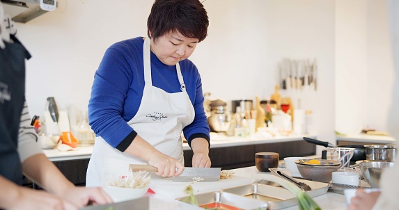 Japanese chef, woman and kitchen with knife, cooking and prepare ingredients for catering services. Person, food and chopping board for nutrition, diet or health with job in restaurant, cafe or diner