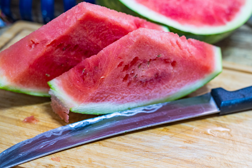 two slices of watermelon on a cutting board next to a knife.
