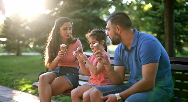 Young Family Eating Ice Cream And Relaxing On The Park Bench