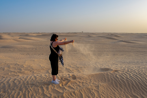 06.11.23 Sahara desert, Tunisia: Side view of young woman, female tourist releasing sand from hands in sahara desert, Tunisia.