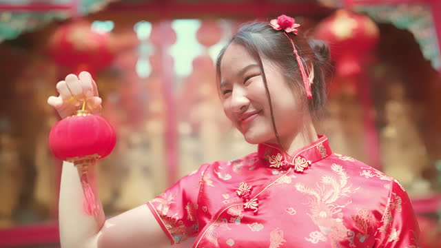 youthful, red-haired Asian girl Cheongsam is playing with a crimson paper lantern.grinning broadly while facing the camera in the Chinese temple.