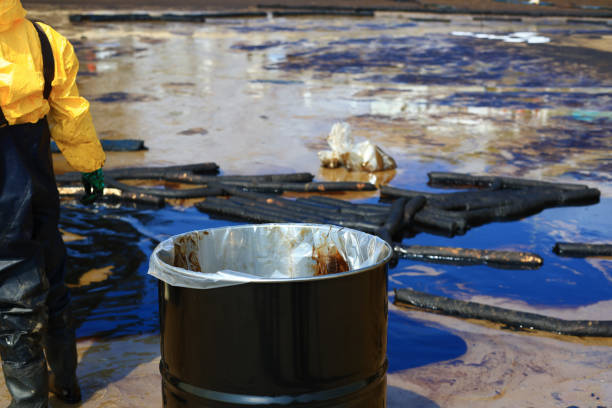 uma pessoa em um traje de proteção caminhando ao longo de uma costa poluída e limpar uma mancha de petróleo bruto - oil slick pouring chemical oil - fotografias e filmes do acervo