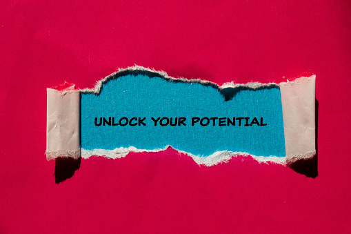 Unlock your potential lettering on ripped red paper with blue background. Conceptual business symbol. Top view, copy space.