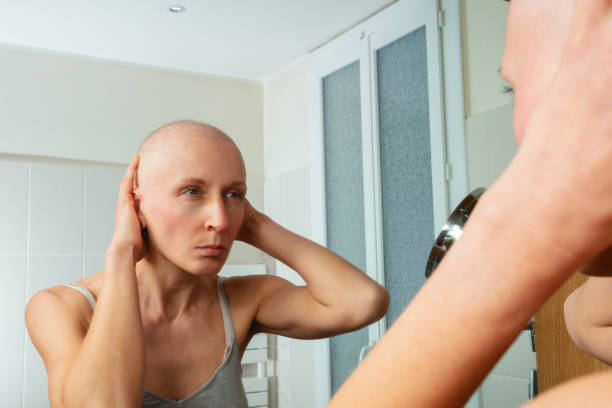 istock Sick woman with shaved head examining self in mirror closely 1993373231
