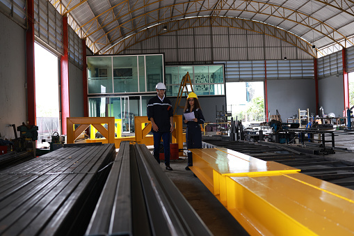 Two technicians  industrial specialist engineers with safety vest uniforms and  helmets using smart digital checking machine maintenance industrial parts industrial engineering concept