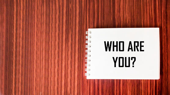 Who are you question written on a notepad and wooden background.