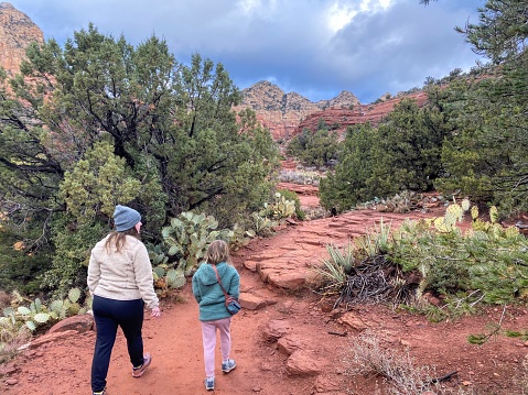 A mother and daughter going for a hike on a winter day in Sedona, Arizona, USA, with the red mountains of Sedona covered in snow in the background.