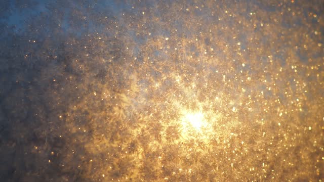 The frosty pattern on window glass occurs due to the condensation of water vapor on glass cooled below 0 degrees. Frost flowers, curls and crystals. Morning yellow-orange low winter sun on the horizon