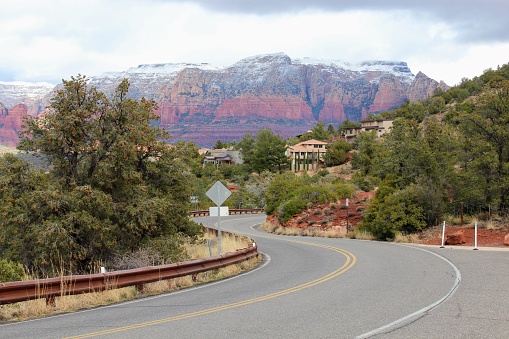 A road with beautiful views of the landscape and town view of Sedona, Arizona in winter, with Sedona surrounded by red-rock buttes, steep canyon walls and pine forests