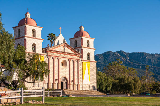 Santa Barbara, CA, USA - April 20, 2009: Old Mission church front facade in sun  under blue sky. Green trees and mountains in back.