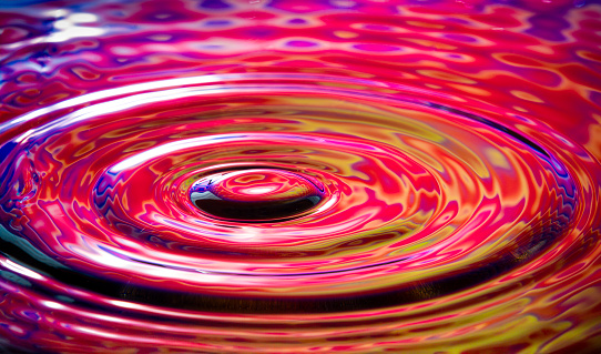 Close up of circular water ripples and colorful reflections.