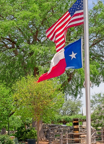 The American and Texas state flags fly over a public park in downtown Fredericksburg Texas. Fredericksburg settled by German immigrants is in the center of the historic Texas hill country.