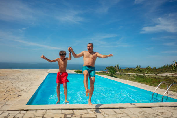 istock Dad and son jump backwards in sunny pool over blue sea horizon 1993473985