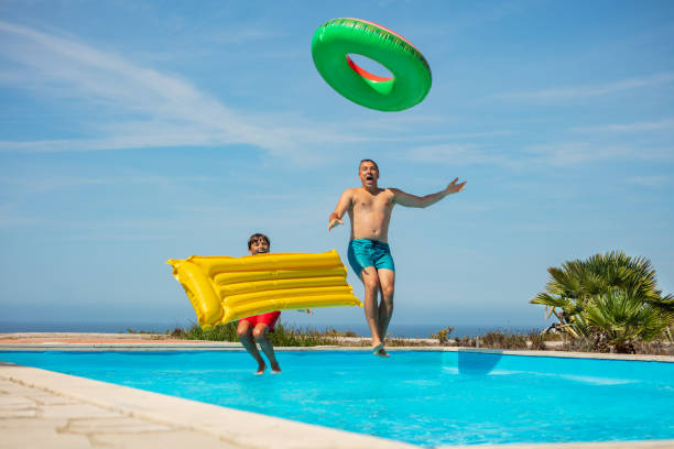 istock Father and son excited jumping into pool with colorful floats 1993473989