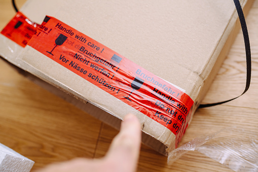 Finger pointing to cardboard box with inscription Handle with care in multiple languages - fragile parcels goods transported via postal services