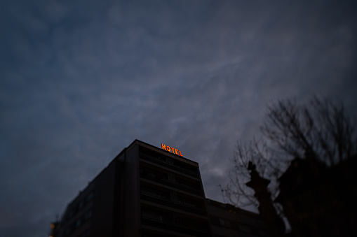 Low angle view of neon hotel word text on the tall inhabited window and dramatic sky