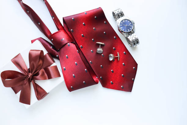 Gift box, necktie, cuff links, and wristwatch against white background.