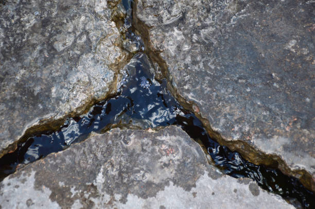 A deep crack in the road surface is filled with water after rain. The old concrete surface on the road was cracked due to weather conditions. dangerous driving on the road