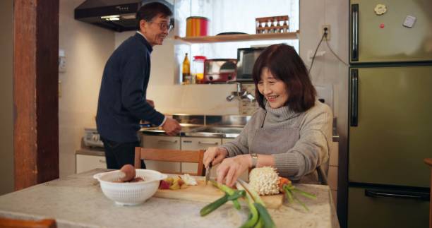 istock Cooking, conversation and Japanese couple in kitchen cutting vegetables for meal, dinner or lunch. Happy, talking and senior man and woman preparing food for supper together with produce at home. 1993530596