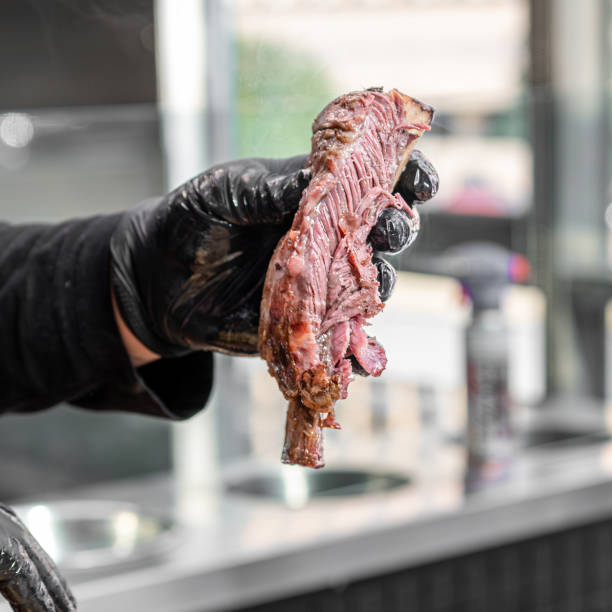the gloved hand of a man holding up an open meat on a grill
