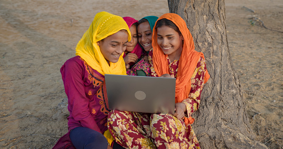 Happy Indian girls using laptop in desert village, Thar Desert, Rajasthan, India.