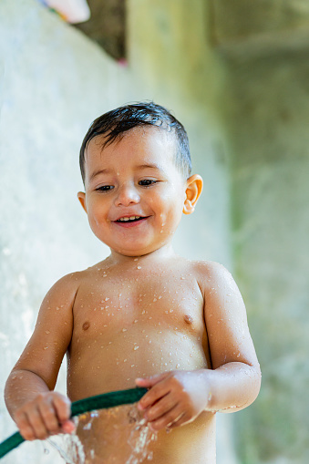 Latino baby boy playing with hose in the field