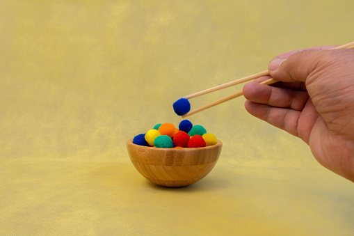 A person selects a blue ball from a wooden bowl using chopsticks, with a concept of choice and copy space