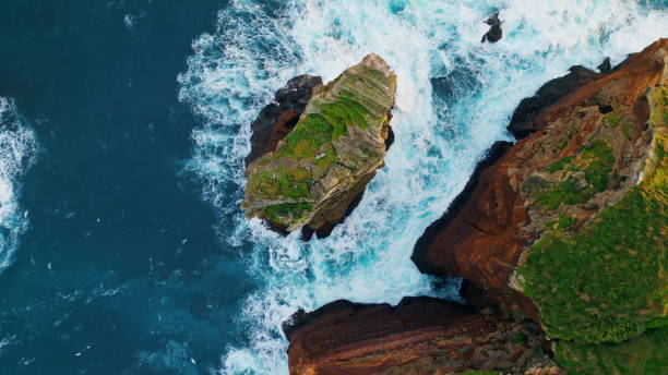 istock Foaming blue water breaking on stone cliff. Aerial stormy rough ocean crashing 1993684769