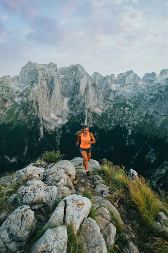 A female skyrunner running and trail running on rocky mountain in wilderness. An extreme sportswoman jogging, running and trail running while mountaineering in wild nature. A skyrnner runs on height.