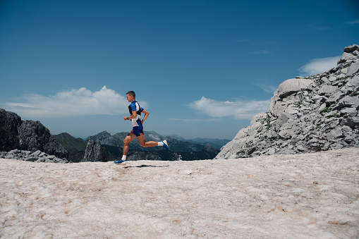 An extreme sportsman is running an ultramarathon, skyrunning and trail running on mountain range on sunny day in wild nature. A skyrunner is running fast a marathon in mountain range. Copy space.