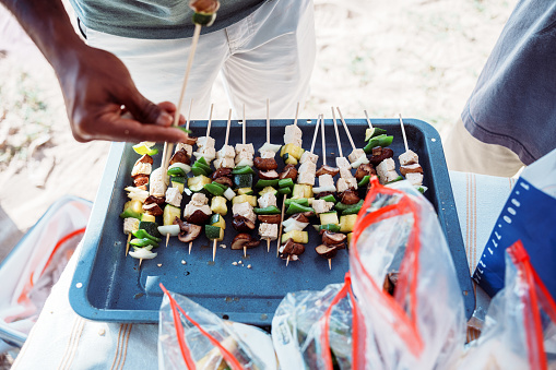 Cropped view of an unrecognizable Indian man preparing kabobs while barbecuing with friends and family at the beach in Hawaii.