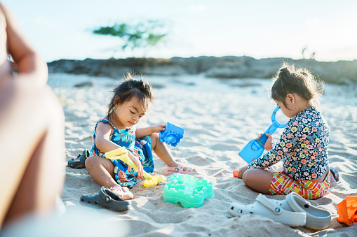 Two adorable toddler girls of Asian descent play in the sand together at the beach in Hawaii.